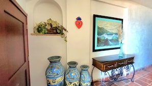 Un couloir avec une porte en bois, une étagère ornée de fleurs séchées, un tableau encadré et trois vases décoratifs.