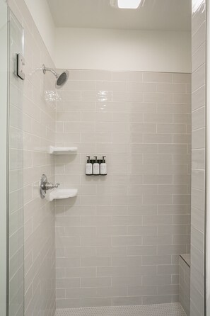 Un petit espace douche fermé, avec des murs recouverts de carreaux blancs et une porte en verre.