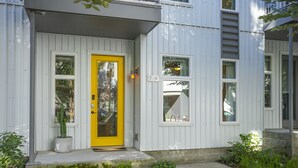 A modern building with a bright yellow door, white exterior walls, and a small garden area with plants.