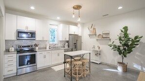 A modern kitchen with stainless steel appliances, white cabinetry, and a central island with stools.