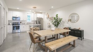 A modern kitchen with white cabinets, stainless steel appliances, and a wooden dining table with benches.