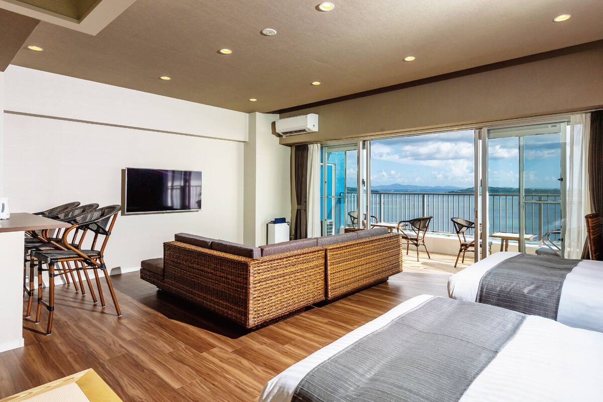 A hotel room with a balcony, a TV, a sofa, and a bed.