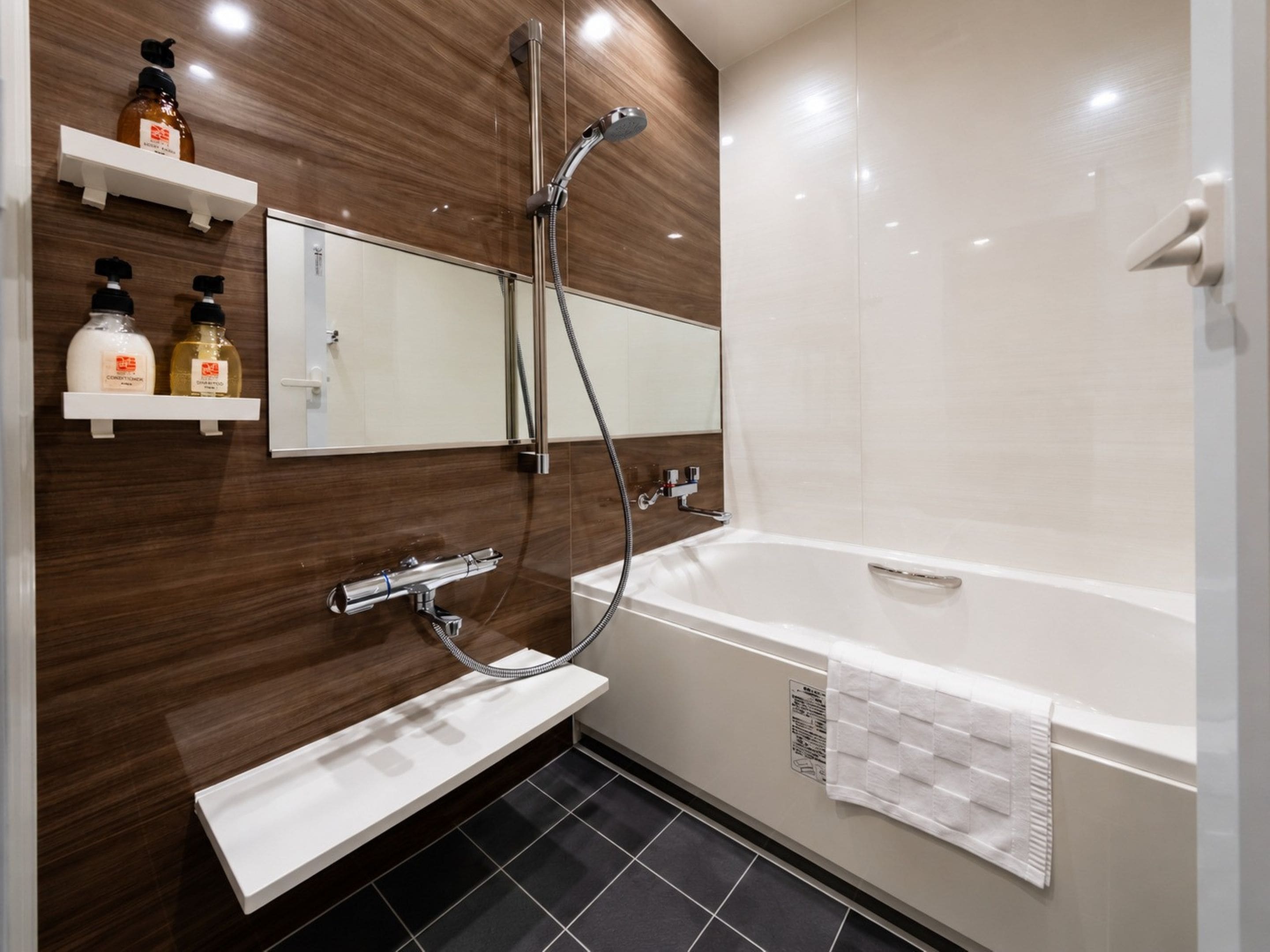Une salle de bain moderne équipée d’une baignoire, d’une douche, d’un meuble-lavabo avec miroir et de deux étagères contenant des articles de toilette.