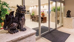 A reception area with a glass door, a reception desk, and two lion statues. - Sunset Resort Canphou (Motobu)
