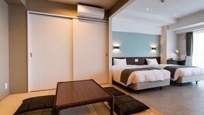 A modern hotel room with a large bed, a separate sofa bed, a small table, and a sliding door closet. - Sunset Resort Canphou (Motobu)