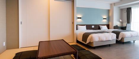 A modern hotel room with a large bed, a separate sofa bed, a small table, and a sliding door closet.