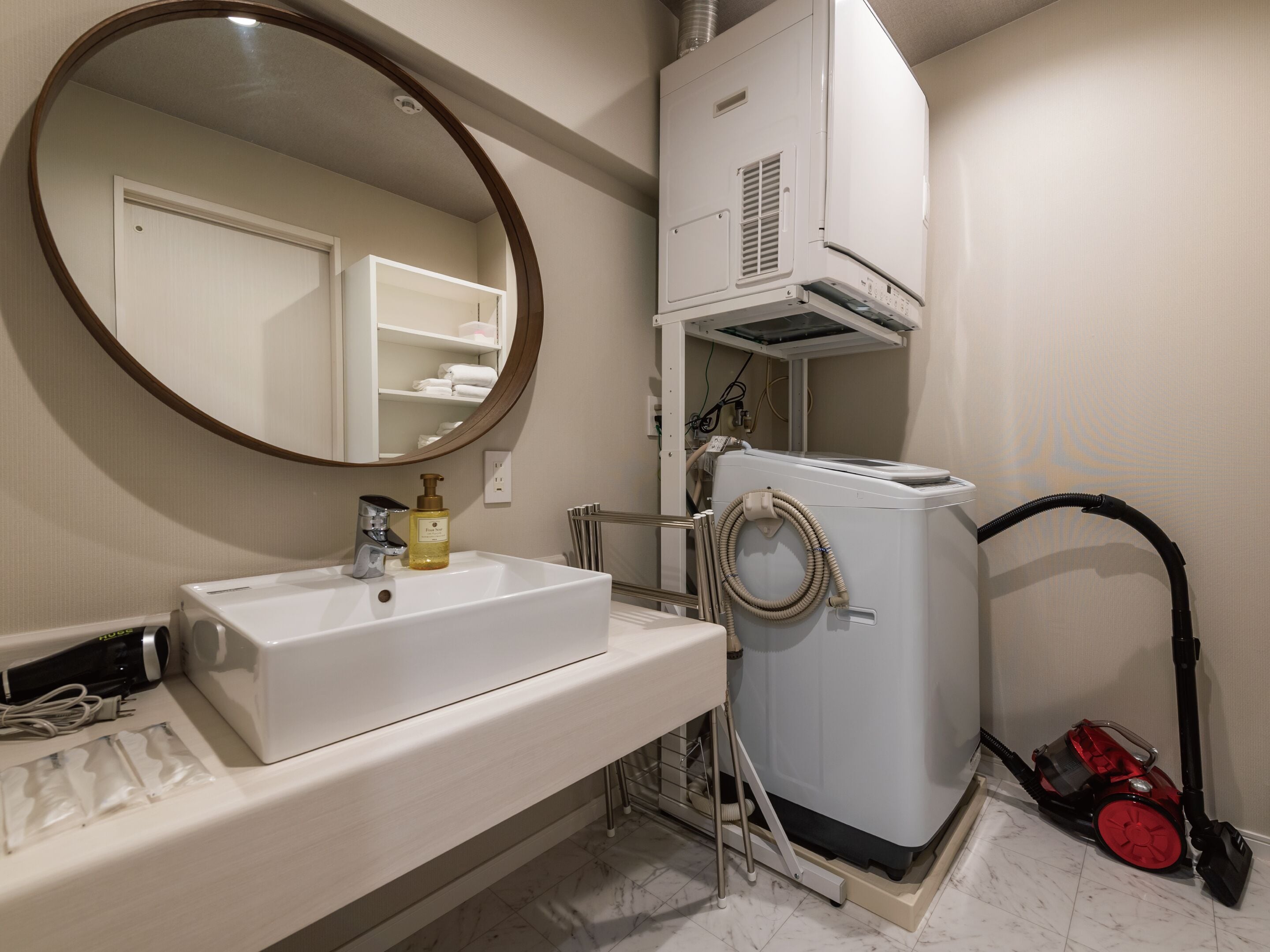 A bathroom with a white sink, a mirror, a white washing machine, and a red vacuum cleaner.