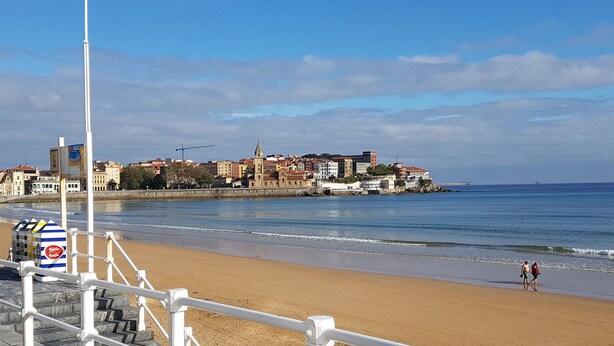 A beach with a white railing, a cityscape in the background, and a clear sky. - San Lorenzo beach front center apartment (Gijón)