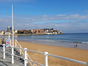 A beach with a white railing, a cityscape in the background, and a clear sky. - San Lorenzo beach front center apartment (Gijón)