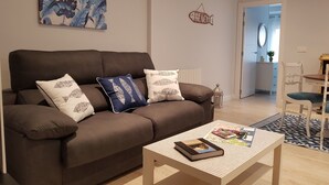 A modern living room with a brown sofa, decorative pillows, a coffee table with a book, and a wall art piece. - San Lorenzo beach front center apartment (Gijón)