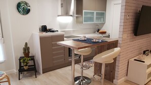 A compact kitchen with a central island, bar stools, a small side table with a cactus, and a TV mounted on a brick wall. - San Lorenzo beach front center apartment (Gijón)