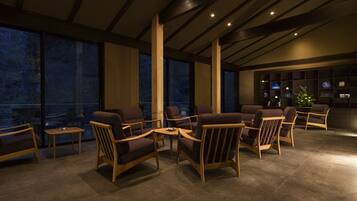 A modern lounge area with wooden furniture and large windows offering views of the outdoors.