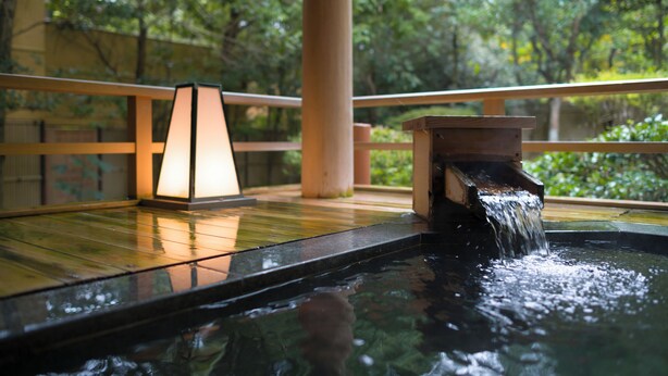 Un área de aguas termales con una terraza de madera, una fuente de agua y una lámpara.