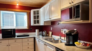 A compact kitchen with white cabinets, a microwave, a coffee maker, and a sink.