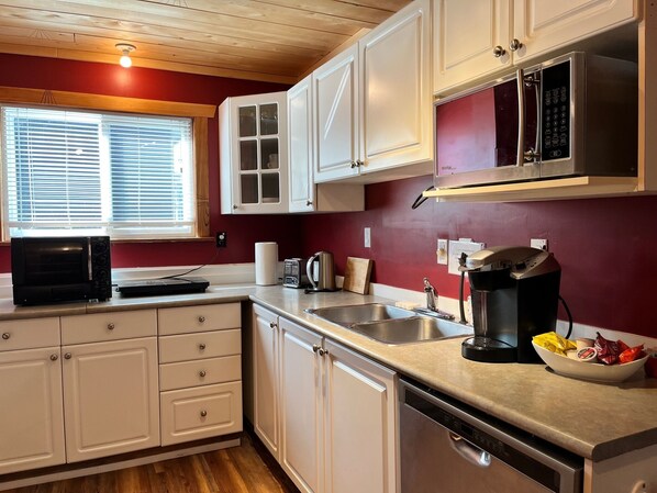 A compact kitchen with white cabinets, a microwave, a coffee maker, and a sink. - Frigon Suite - Waterfront (Port Alice)
