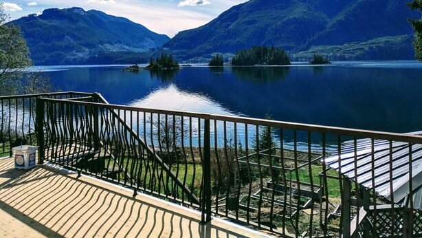 A lakeside view with a wooden deck, metal railing, and a clear sky.