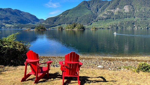 Two red Adirondack chairs facing a lake with mountains in the background. - Frigon Suite - Waterfront (Port Alice)