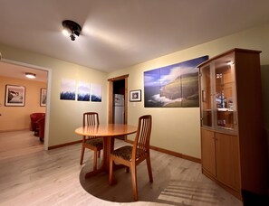 A dining area with a round table and chairs, a cabinet with glass doors, and framed pictures on the wall. - Frigon Suite - Waterfront (Port Alice)