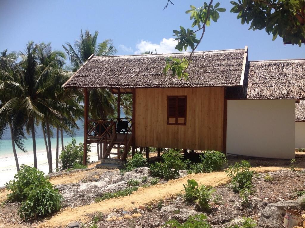 Una cabaña de playa de madera con techo de paja, una terraza de madera y vista al océano.