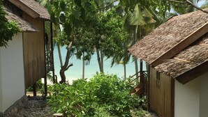 A secluded beach area with thatched-roof huts, lush greenery, and a clear view of the turquoise sea. - BaraCoco Bungalows (Bira)