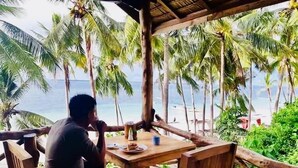 A wooden table and chairs with a view of the beach and palm trees. - BaraCoco Bungalows (Bira)