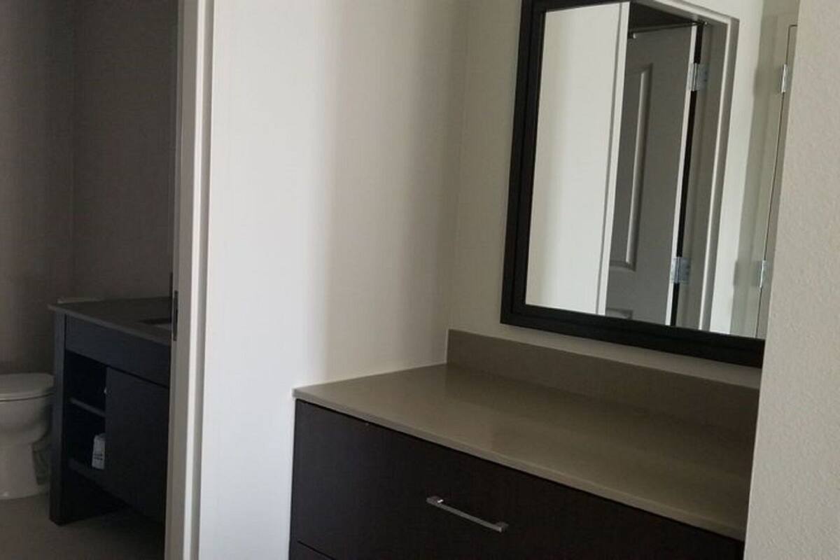 Un baño con inodoro, un tocador oscuro con espejo y un perchero para toallas.