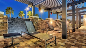 An outdoor lounge area with sun loungers, a stone wall, and palm trees. - Residence Inn by Marriott Corpus Christi Downtown (Corpus Christi)