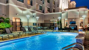 A swimming pool with lounge chairs and a bar area, surrounded by a multi-story building with balconies.
