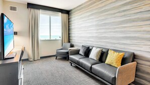 A modern hotel room with a leather sofa, a small round table, a TV, and a large window with curtains. - Residence Inn by Marriott Corpus Christi Downtown (Corpus Christi)