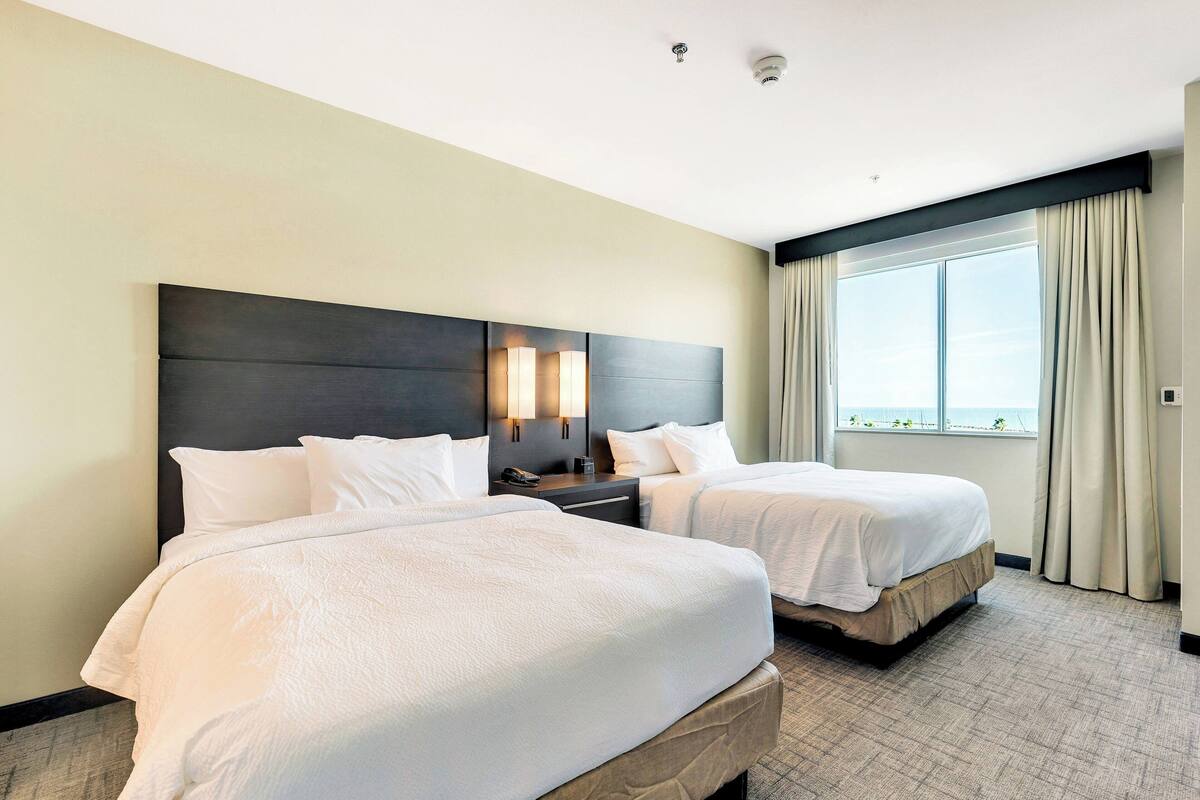 Una habitación de hotel con dos camas, un ventanal con cortinas y un cabecero moderno.