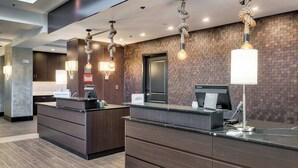 A hotel reception area with a modern design, featuring a brick wall, a reception desk, and a digital screen. - Residence Inn by Marriott Corpus Christi Downtown (Corpus Christi)