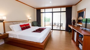 Habitación de hotel con una cama grande, un escritorio, una silla, un televisor y un balcón con una mesa y sillas.