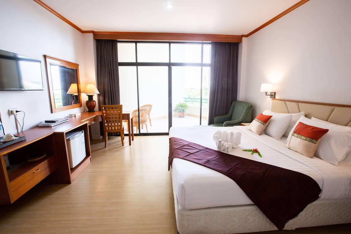 A hotel room with a bed, a desk with a computer, a chair, a TV, and a balcony with a view.
