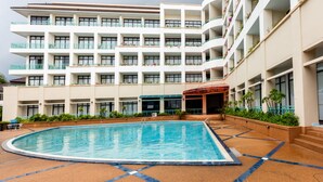 Un hotel con piscina, varios balcones con plantas y un área cubierta.
