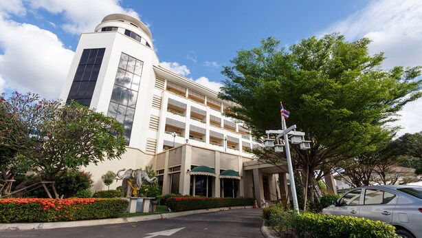 Un hotel de varios pisos con un diseño arquitectónico moderno, que destaca una imponente torre cilíndrica y una entrada ajardinada con una estatua.