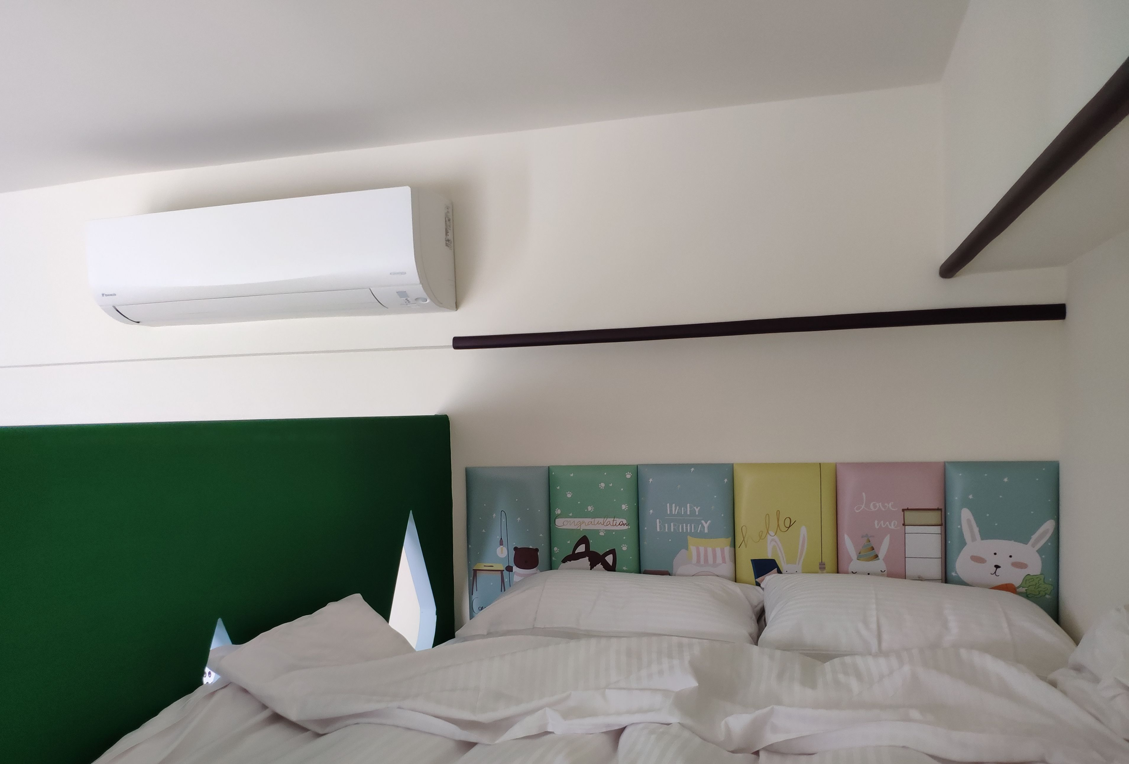 A neatly made bed with white linens, a green headboard, and a wall-mounted air conditioner.