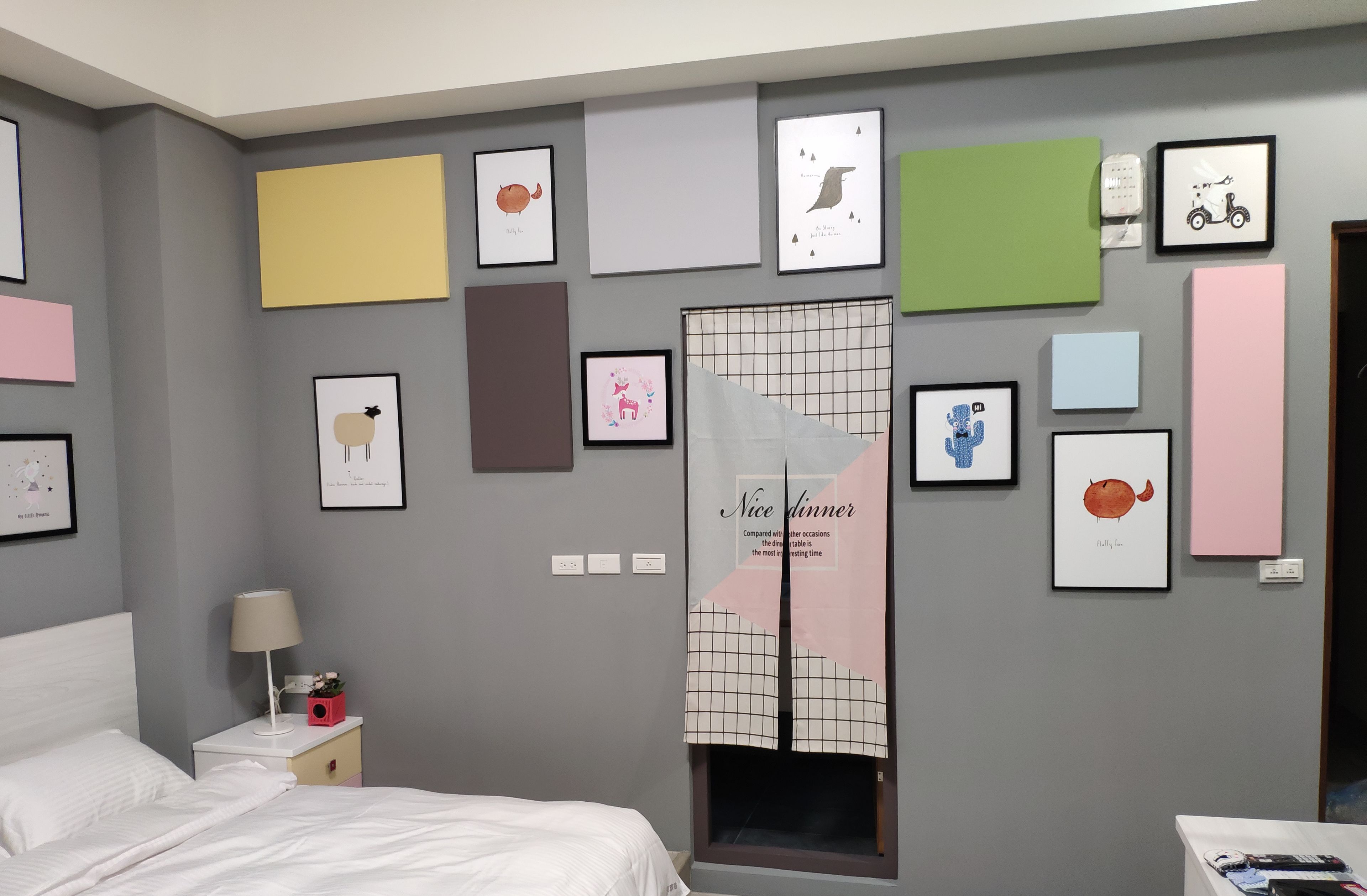 A bedroom with a bed, bedside table, lamp, and a wall decorated with various framed pictures and a mirror.