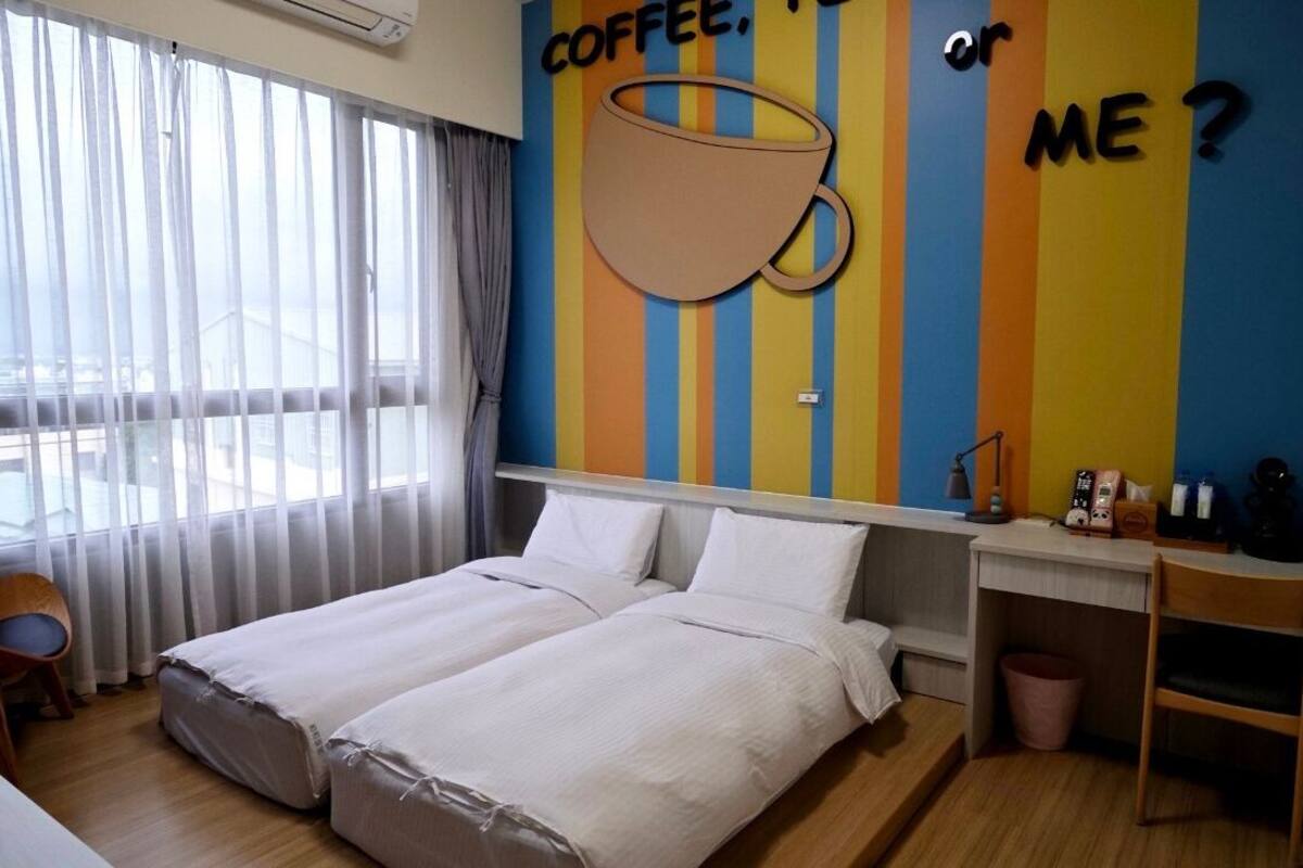 A hotel room with two beds, a desk, and a large window with curtains.