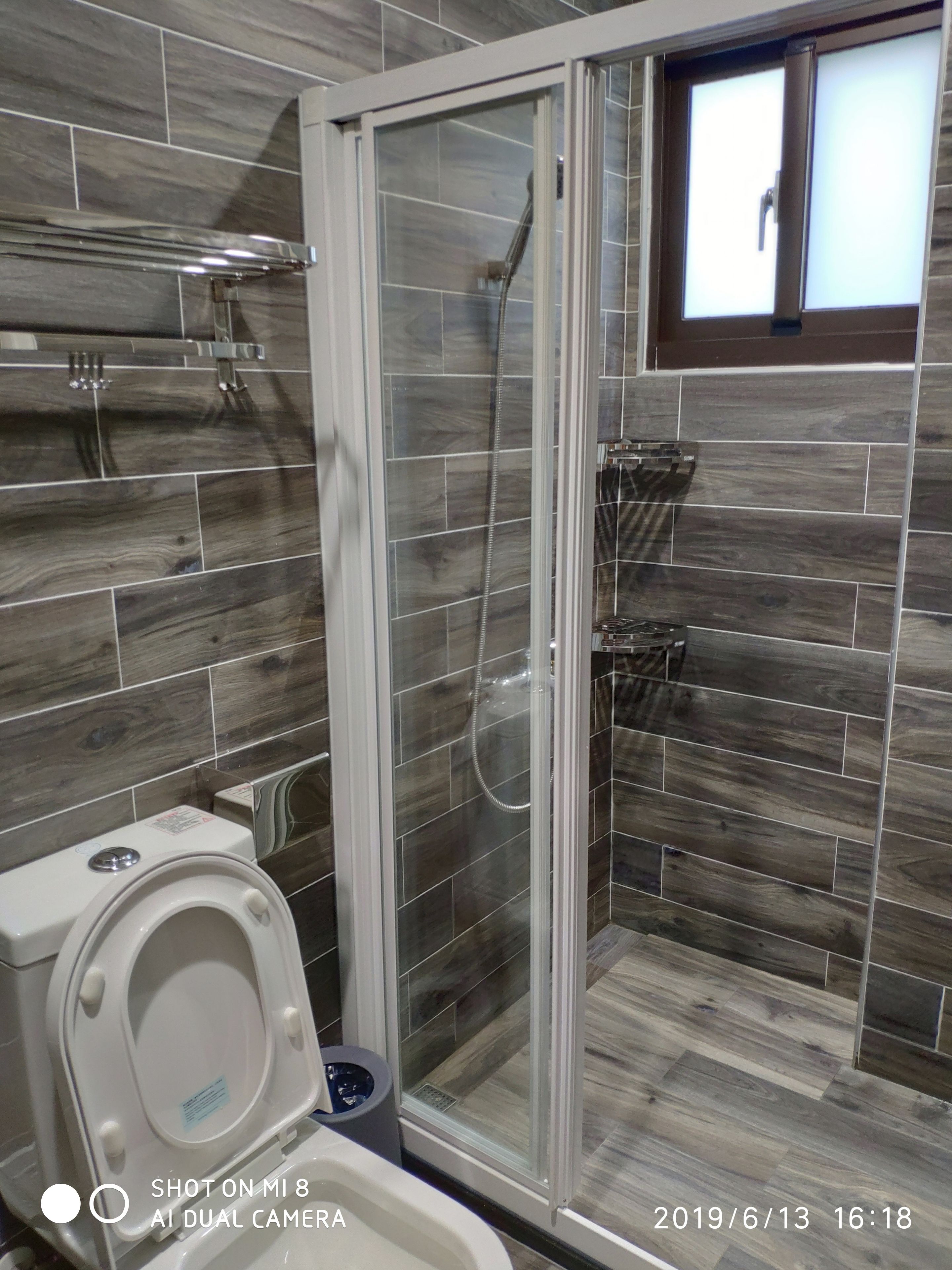 A bathroom with a glass-enclosed shower, a toilet, and a small window.