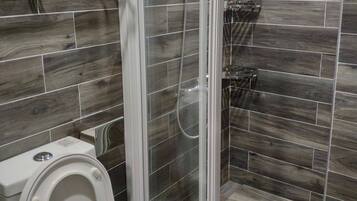 A bathroom with a glass-enclosed shower, a toilet, and a small window.