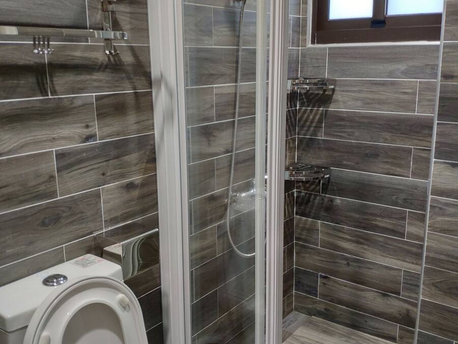 A bathroom with a glass-enclosed shower, a toilet, and a small window.
