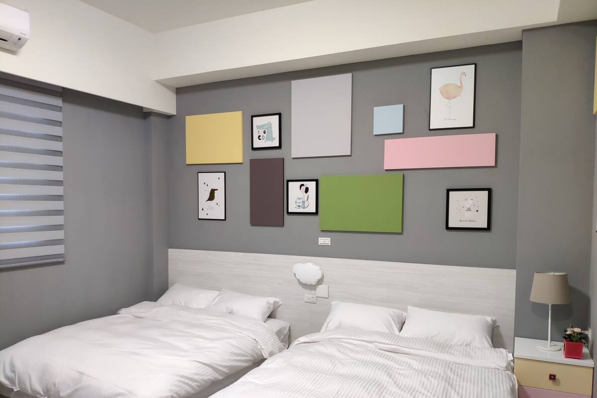 A hotel room with two beds, a bedside table with a lamp, and a wall decorated with various framed pictures.