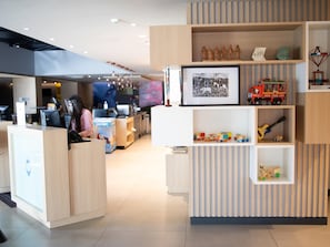 Un comptoir d’accueil avec un ordinateur, une personne derrière le comptoir, et une vitrine contenant des figurines et un tableau encadré.