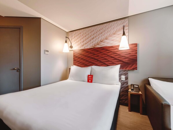 A hotel room with a bed, bedside table, and a wall-mounted telephone.