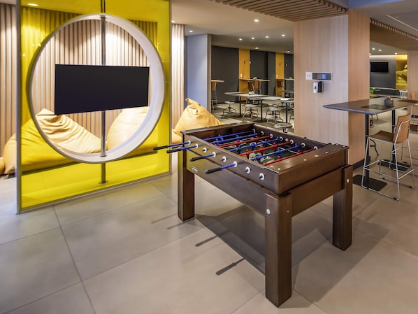 A modern indoor setting with a foosball table, seating area, and a TV screen. - Ibis Juazeiro do Norte (Juazeiro do Norte)