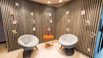 A room with two grey chairs, a small orange table, and a vertical striped wall with various notes.