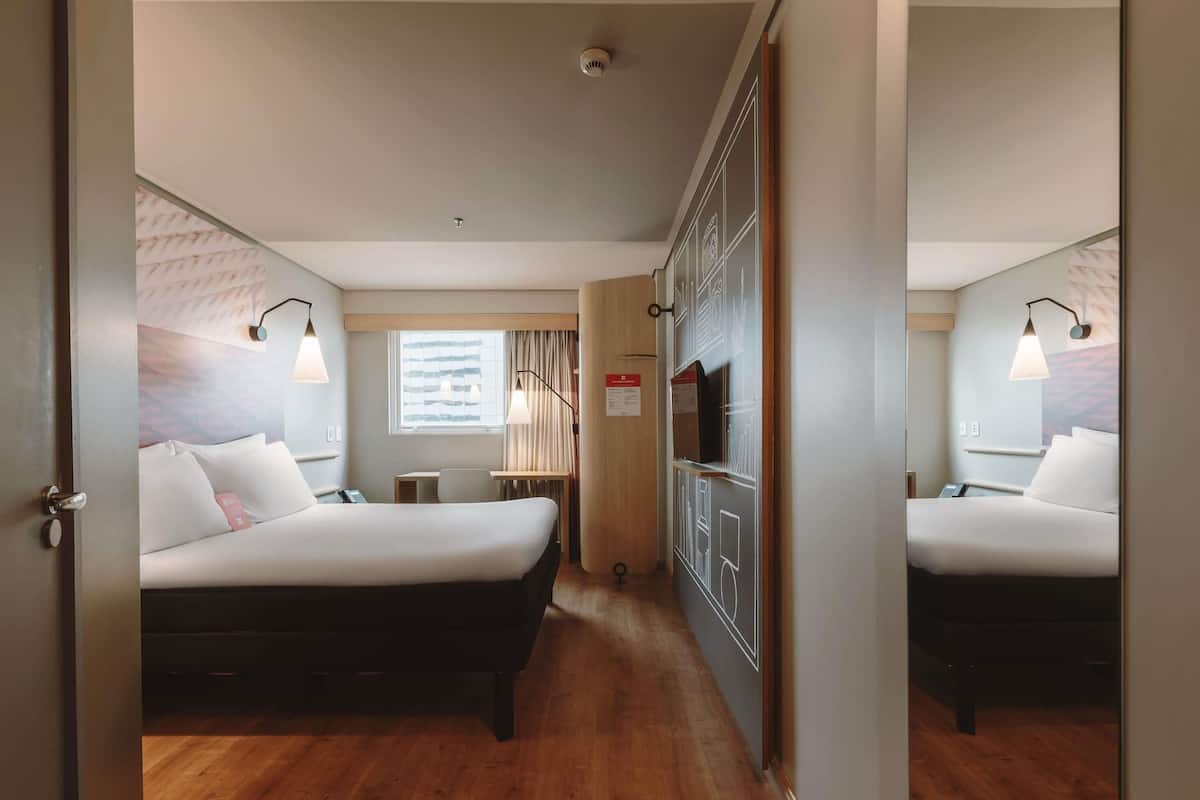 Ein Hotelzimmer mit Bett, Nachttisch, Lampe und Spiegel.