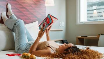 Eine Person liegt im Bett mit einem Buch, einem Hamburger und einem Glas Wasser.