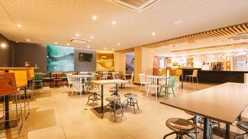 A modern restaurant interior with high ceilings, recessed lighting, and a variety of seating options including tables and chairs.
