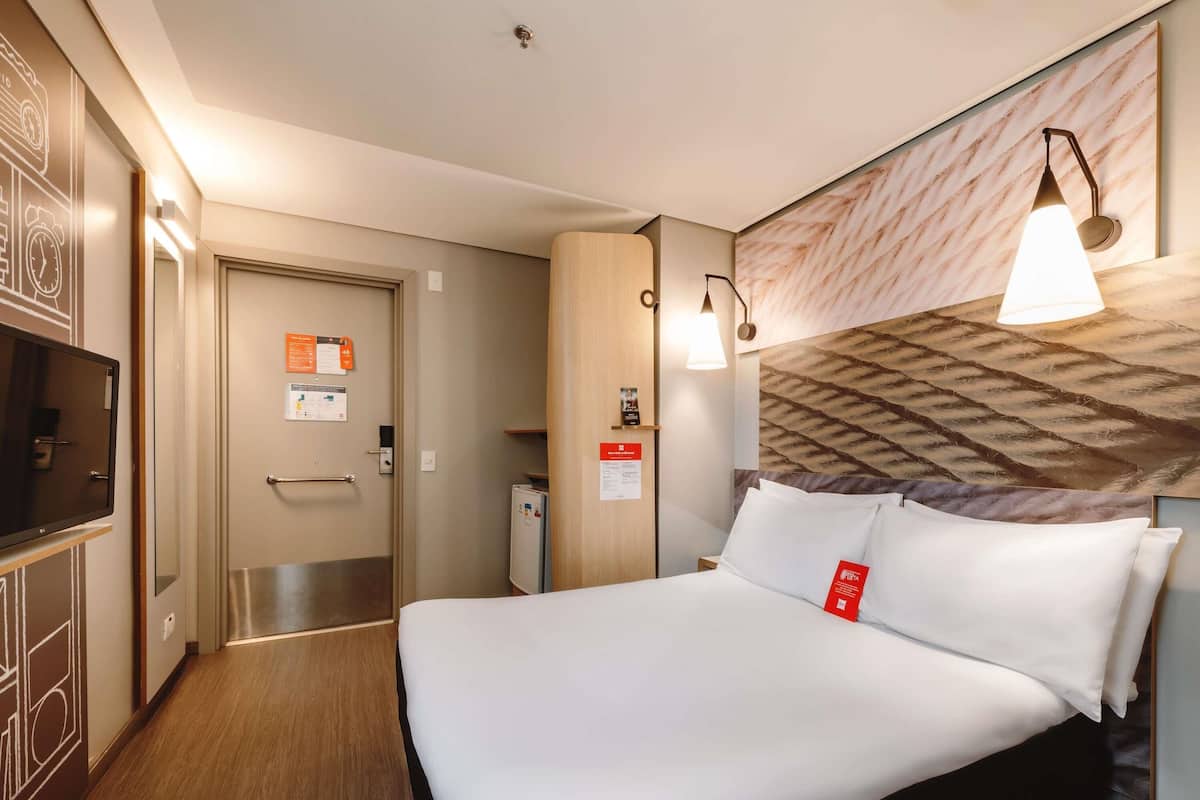 Ein Hotelzimmer mit einem Bett, einem Fernseher, einer Tür und einer Wandleuchte.